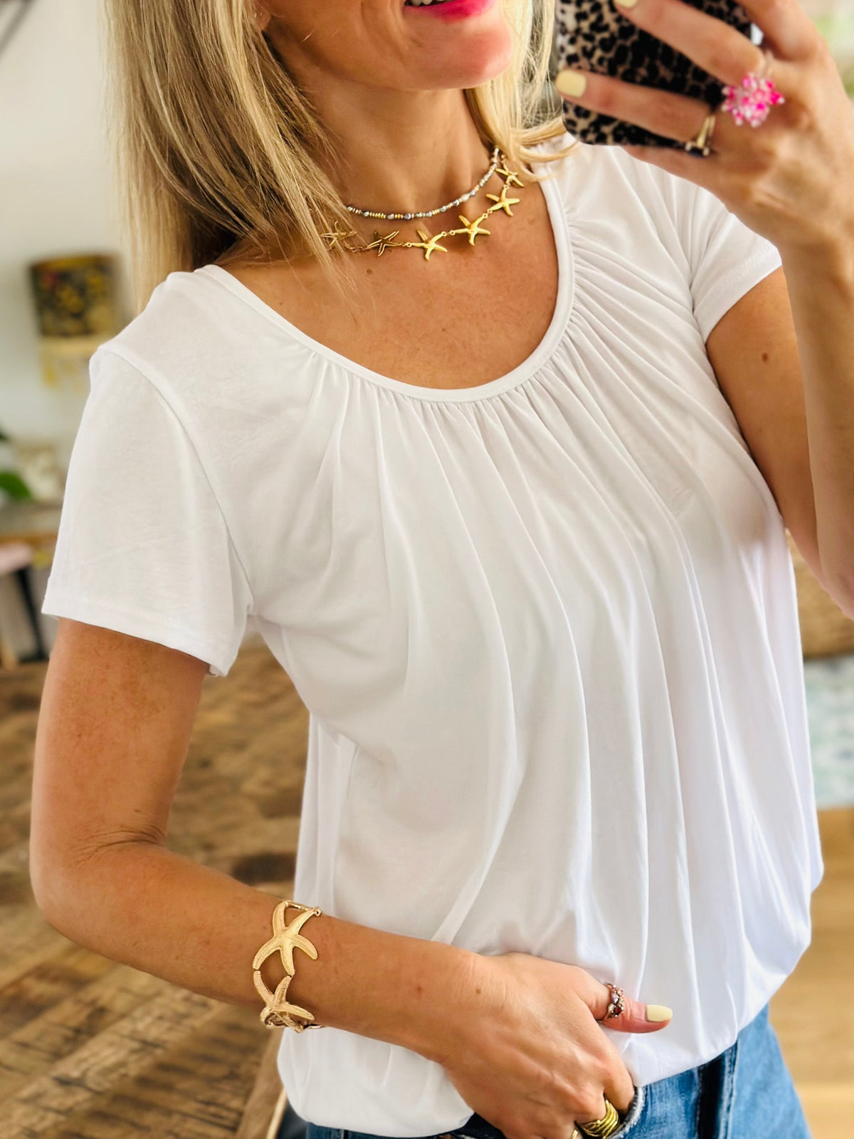 Woman taking a mirror selfie wearing a white top and blue jeans indoors.
